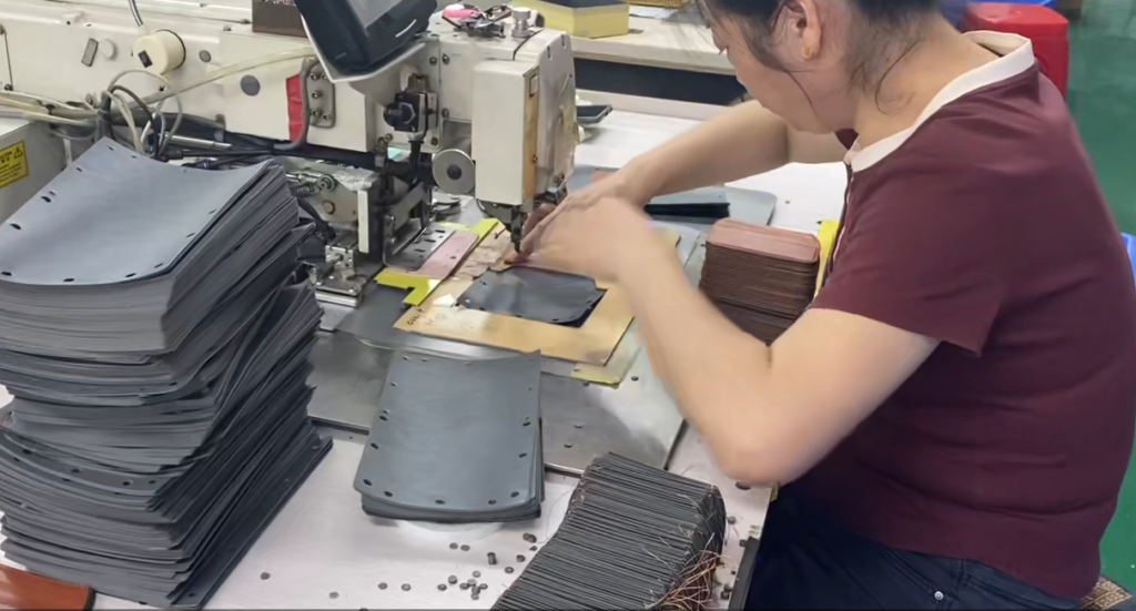 Worker sewing a gray camera case beside a stack of matching case panels